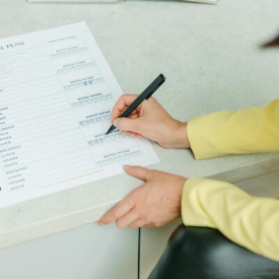 Woman writing on a weekly meal plan checklist indoors, focusing on diet organization.